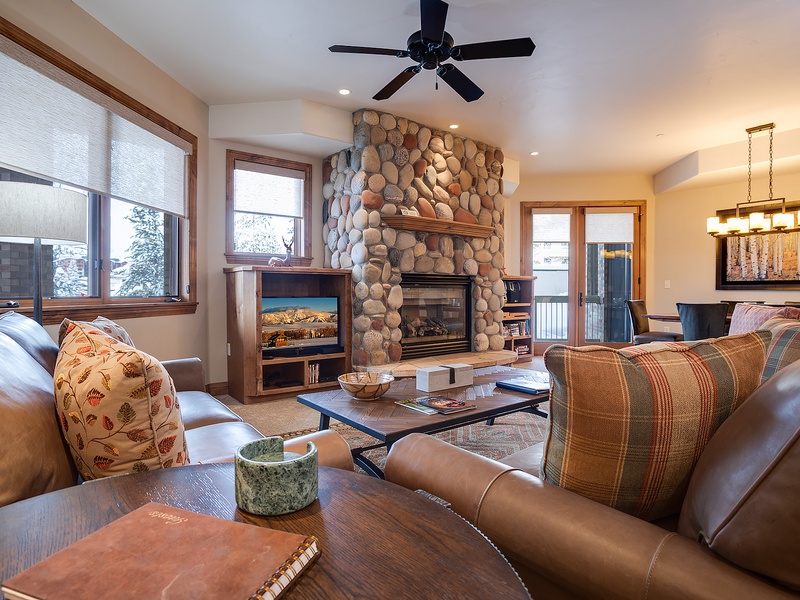 Sink into plush leather sofas in your cozy living room, where a stunning river-rock fireplace and mountain views through expansive windows create the perfect retreat after a day of adventure.