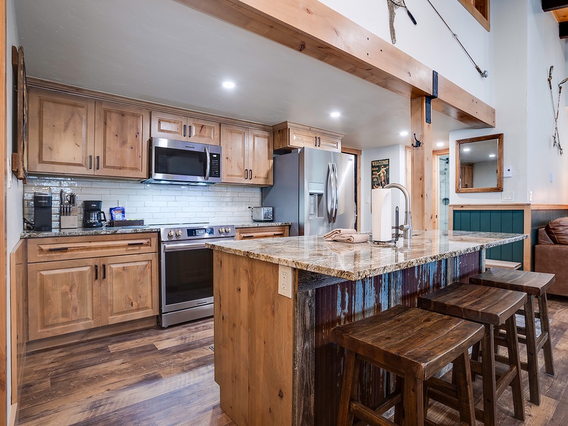 Your mountain retreat features a fully equipped gourmet kitchen with granite island seating, stainless appliances, and rustic wood accents beneath soaring timber-beam ceilings.