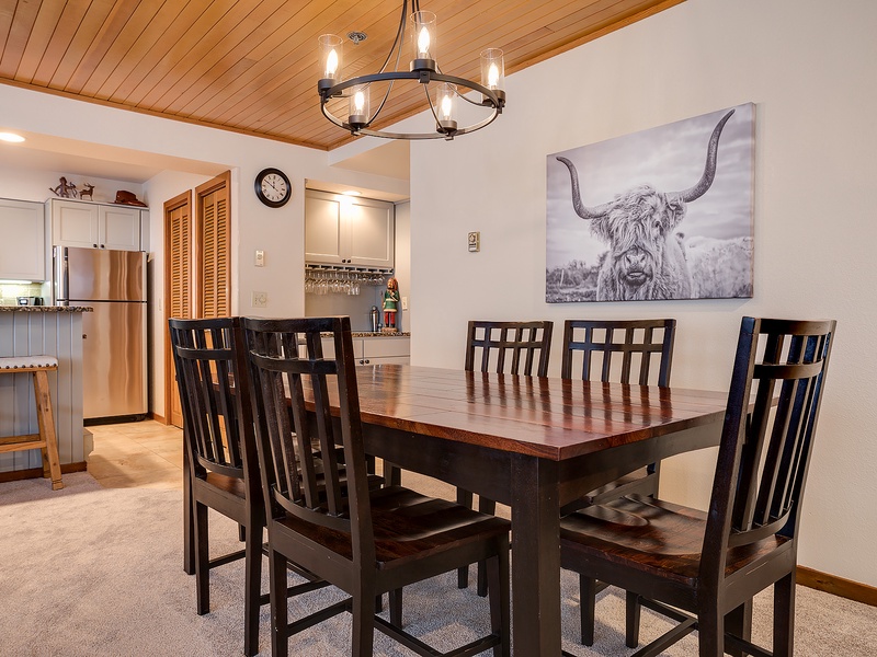 Gather around this inviting dining table where your group can share meals and make memories together. The rustic chandelier and warm wood ceiling add mountain charm to every dining experience.