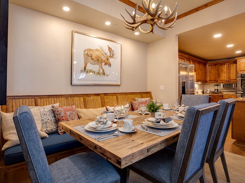 Gather around this warm dining space featuring rustic wood accents, comfortable seating, and a stunning antler chandelier overhead. The open layout flows into a fully-equipped kitchen, perfect for memorable meals together.