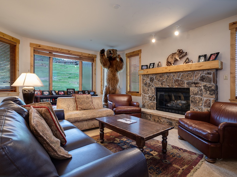 Gather around the stone fireplace in this inviting living room, where rustic charm meets comfort. Large windows frame mountain views while leather seating and warm wood tones create your perfect retreat.
