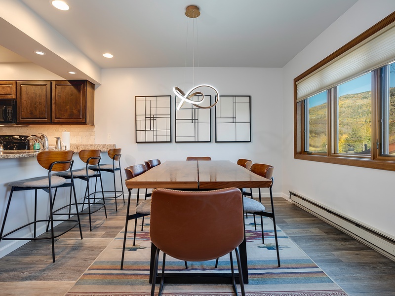 Your open-concept kitchen and dining area invites you to gather around the modern table with stunning mountain views through wide windows, perfect for morning coffee or evening meals together.