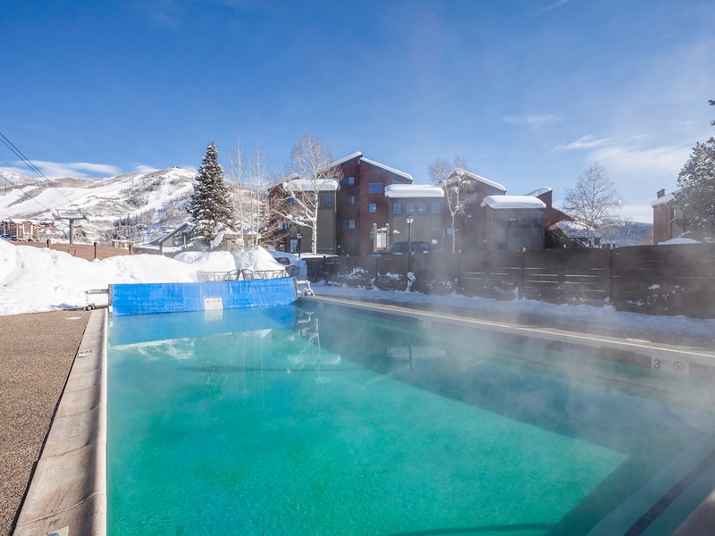 Heated outdoor pool surrounded by snow-dusted mountains and evergreens in a scenic winter resort setting.