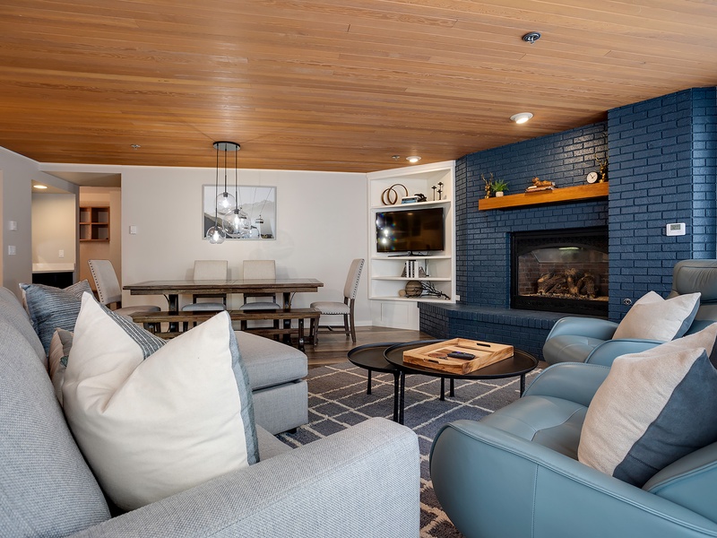 Unwind in your spacious living area with a stunning fireplace, warm wood-paneled ceiling, and cozy seating where you can relax after a day of adventure.