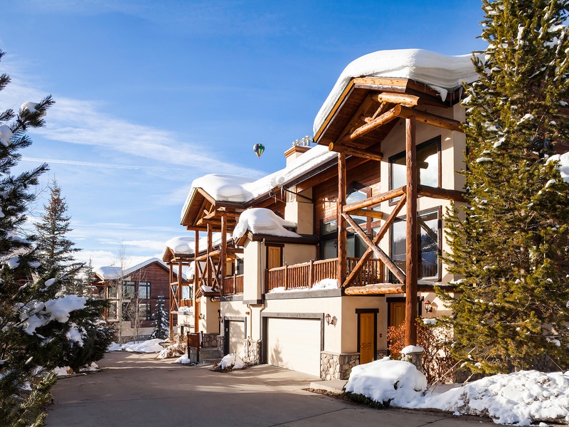 A stunning alpine retreat nestled among evergreens, showcasing rustic timber detailing and snow-dusted balconies, with mountain vistas and bright winter skies setting the stage for your getaway.