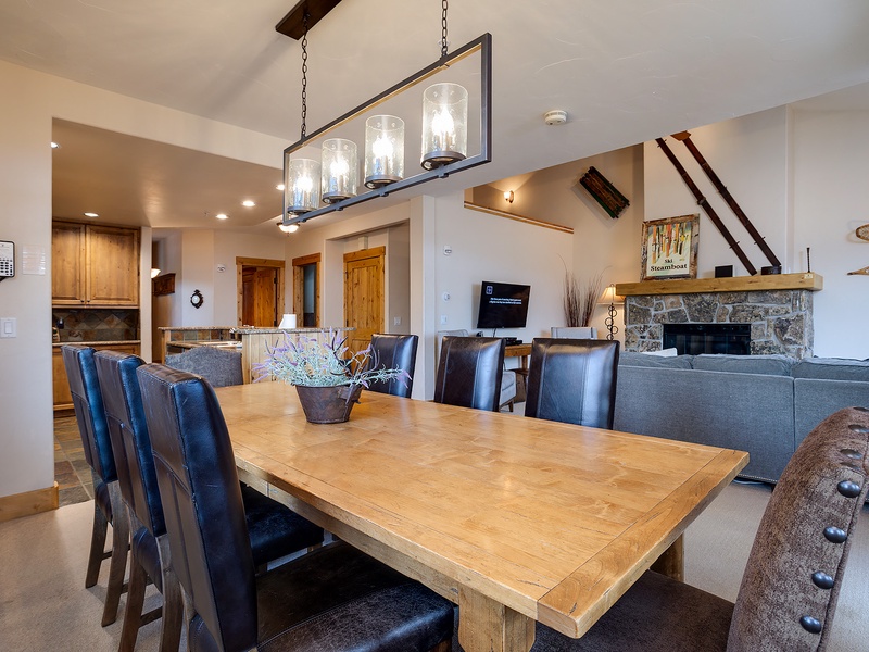 Gather around this spacious dining table where you'll enjoy meals together under warm lighting. The open layout connects to your cozy stone fireplace and well-equipped kitchen, perfect for memorable evenings.