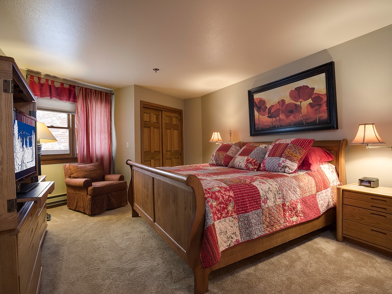 Settle into your cozy bedroom with warm wood furnishings, a plush quilted bed, and soft lighting that invites restful nights after mountain adventures.