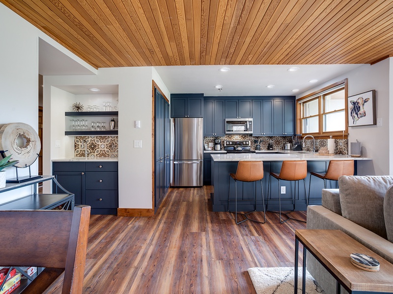 Your open-concept retreat welcomes you with rich wood floors, striking blue cabinetry, and a cozy breakfast bar—perfect for morning coffee or gathering with friends after a day of adventure.