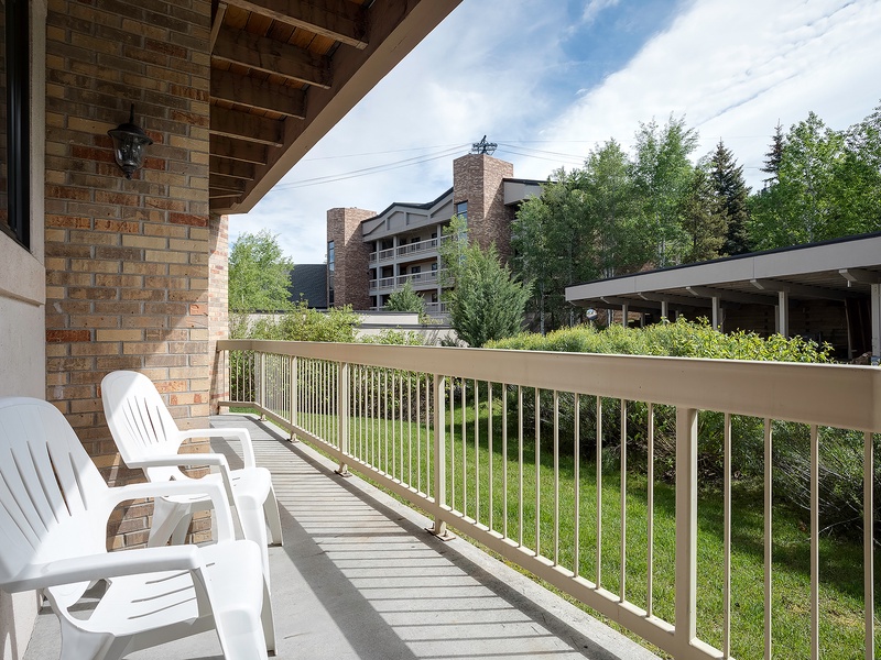 Private balcony overlooking green lawns and neighboring buildings, featuring comfortable seating where you can unwind and enjoy the peaceful surroundings in the fresh air.