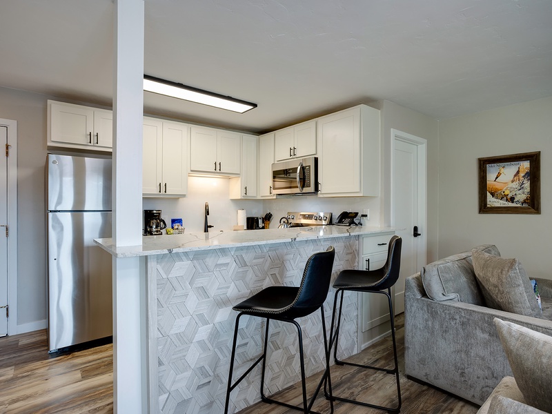 Your open-concept kitchen features white cabinetry, stainless steel appliances, and a stylish breakfast bar with marble-patterned tile backsplash—perfect for morning coffee or casual meals.