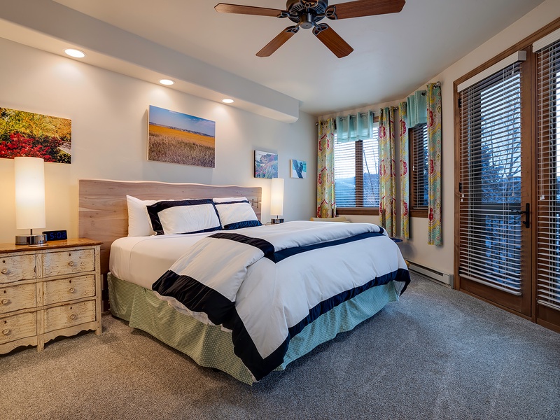 Sink into crisp linens and let the ceiling fan's gentle breeze lull you to sleep. Natural light floods through windows framing mountain views, while colorful artwork adds warmth to your peaceful retreat.