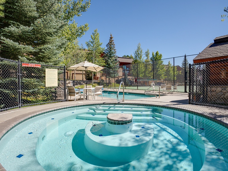 Soak in the bubbling hot tub under sunny skies, with lounge chairs and towering evergreens creating your perfect outdoor escape.