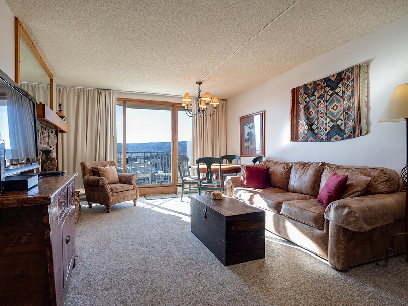 Sink into your spacious living room featuring a plush leather sofa, rich wood furnishings, and southwestern décor. Natural light floods through your private balcony doors, framing stunning mountain vistas that invite you to unwind in style.