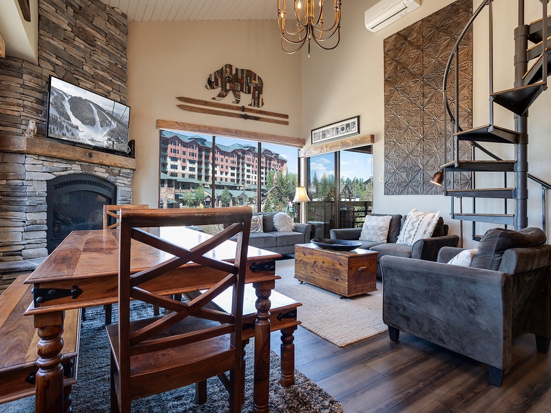 Your mountain retreat features soaring ceilings, rustic stone fireplace, and plush seating that invites you to unwind. Large windows frame stunning views, while the spiral staircase adds a charming loft touch.