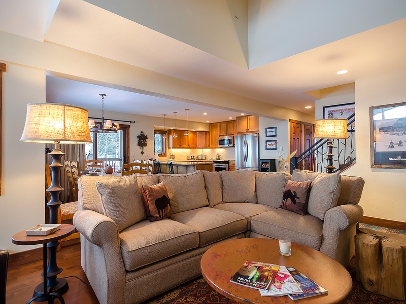 Settle into your spacious living area where plush seating and warm wood tones create an inviting retreat. Beyond, your fully equipped kitchen awaits, ready to make every meal at home feel special.