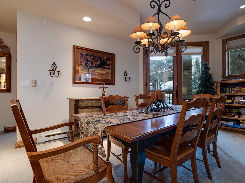 Gather around this inviting dining table where your group can share meals and stories beneath an elegant chandelier. Natural light pours in through windows that frame peaceful mountain views.