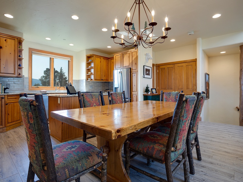 Gather around a handcrafted wood table under elegant chandelier light, with mountain views through the window. This warm, inviting dining space is perfect for shared meals and lasting memories.