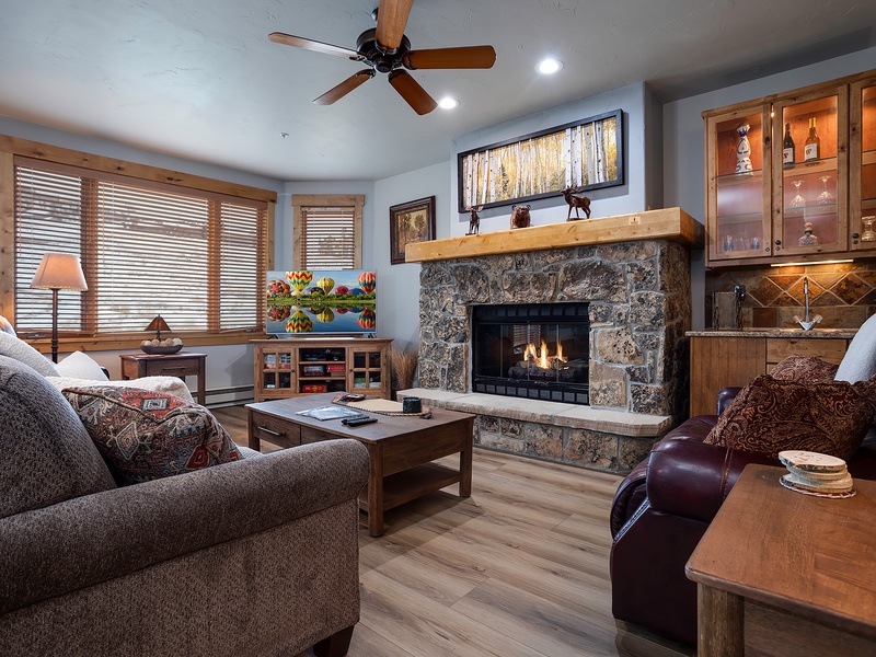 Unwind in your cozy living room with plush seating, a warm stone fireplace, and charming mountain-inspired décor that invites you to relax and feel at home.