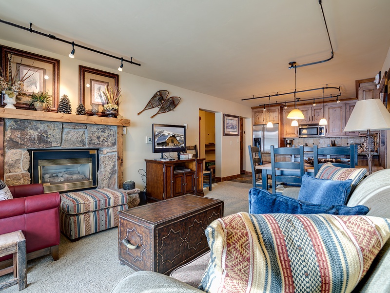 Settle into your cozy mountain retreat with rustic charm: a crackling stone fireplace, inviting seating, and an open kitchen ready for your alpine adventures.