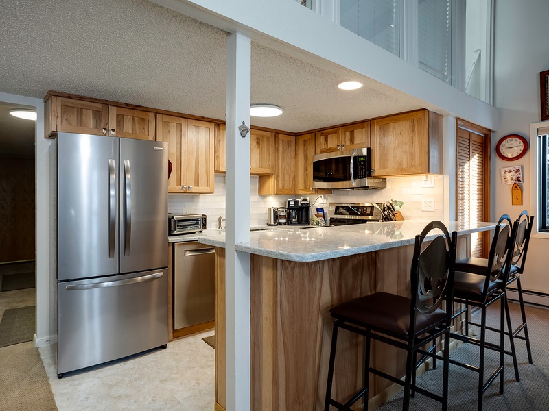 Your fully equipped kitchen features stainless steel appliances, warm wood cabinets, and a breakfast bar perfect for morning coffee or casual meals together.