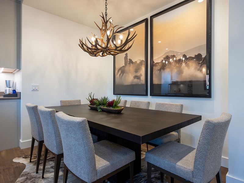 Gather around this striking dining table beneath a rustic antler chandelier, where your group can enjoy home-cooked meals together in a bright, modern space that blends warmth with style.