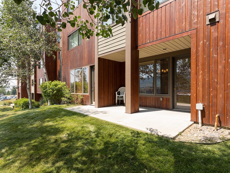 Charming wood-paneled exterior with private patio and lush green lawn, framed by mature trees and offering peaceful waterfront glimpses—your perfect retreat awaits.