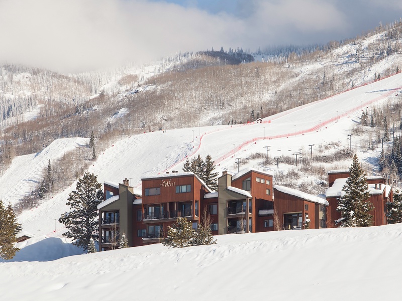 A snow-covered mountain lodge nestled near ski slopes, with chairlifts and pristine powder-covered terrain stretching across the peaks—an ideal winter escape for alpine adventure.