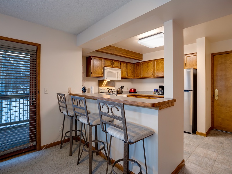 Gather at your breakfast bar with morning coffee, where warm wood cabinetry and a fully equipped kitchen invite you to cook and connect in relaxed comfort.