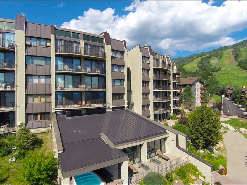 Aerial view captures the property nestled in a mountainside community with ski slopes, summer greenery, and neighboring buildings defining this alpine vacation destination.