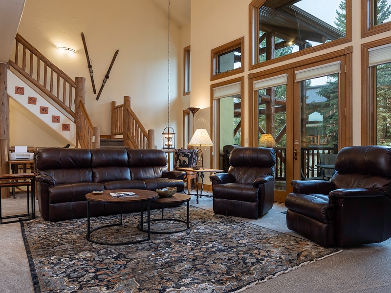 Sink into plush leather seating in your spacious living room, where floor-to-ceiling windows frame lush forest views and a warm, inviting atmosphere welcomes you home.