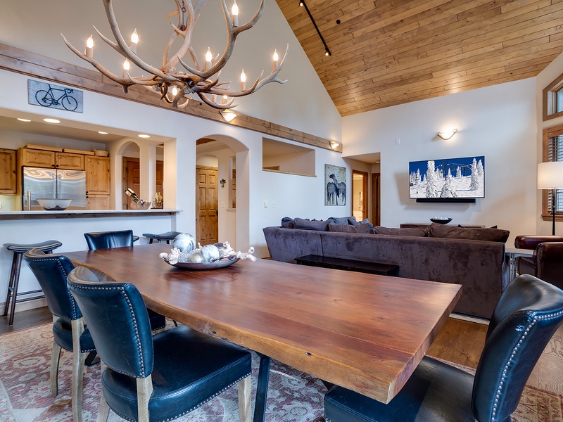Gather around the handsome wood table under a stunning antler chandelier, where high ceilings and warm wood accents create a cozy yet spacious retreat for your group.