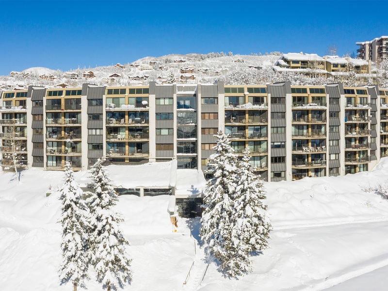 A stunning winter wonderland setting with pristine snow-covered slopes and frosted evergreens surrounding this alpine property. Ski-in/ski-out access awaits against a perfect blue sky backdrop.