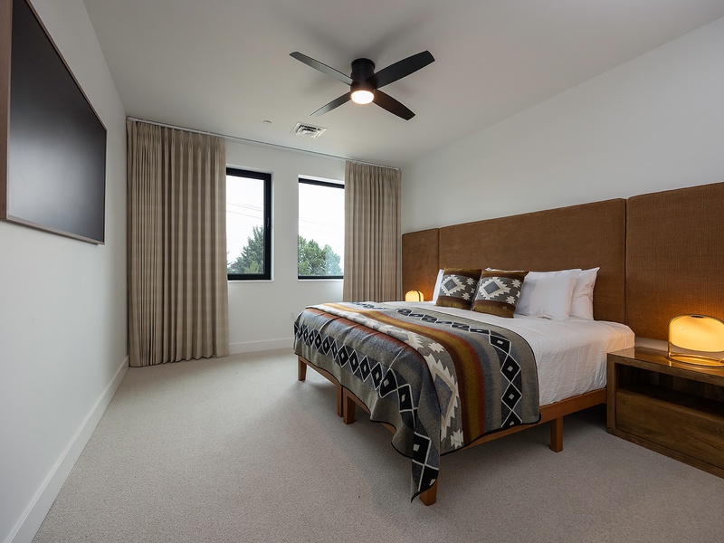 Your modern bedroom awaits with a plush bed, warm lighting, and a ceiling fan to keep you comfortable. Natural light spills through the windows, creating a serene space to unwind after your day.