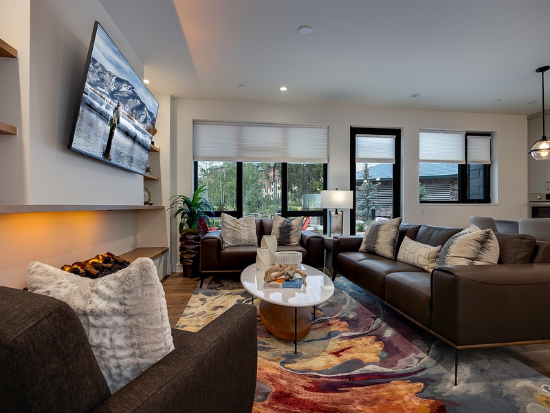 Sink into plush leather sofas and unwind by the glowing fireplace—your perfect retreat after a day of adventure. Sunlight streams through tall windows, bathing the open living space in warmth.