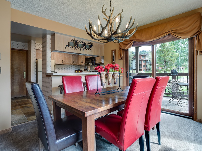 Gather around this rustic dining table under a striking antler chandelier, where your mountain getaway meals become memorable moments. The open kitchen and balcony access create the perfect flow for entertaining.