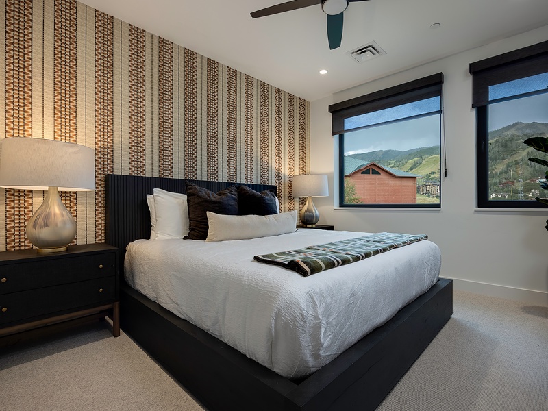 Drift off in crisp linens beneath a striking textured accent wall, with mountain views framing your mornings through large windows. Your peaceful retreat awaits with stylish furnishings and a serene ambiance.