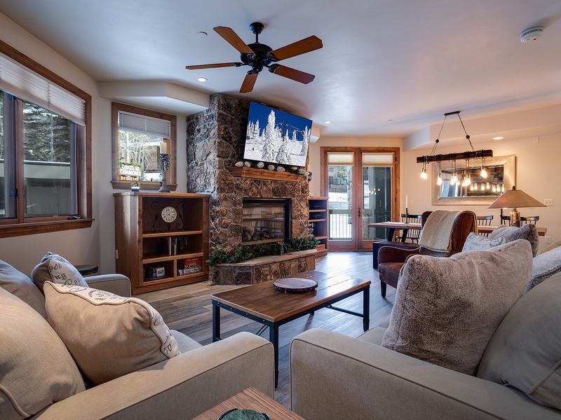 Unwind in your inviting living room with plush seating, a stunning stone fireplace, and natural light streaming through large windows. Your perfect mountain retreat awaits.