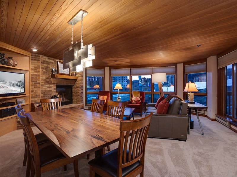 Gather with loved ones in this warm, wood-paneled retreat featuring a cozy fireplace, spacious dining table, and stunning mountain views through expansive windows.