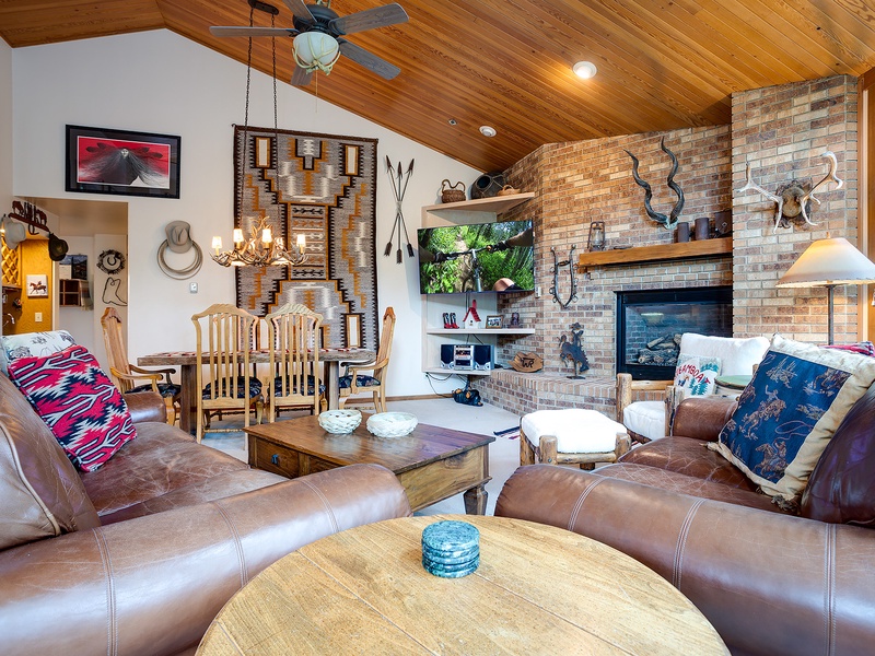 Sink into plush leather sofas in a striking vaulted living room where rustic charm meets modern comfort. Rich wood ceilings, exposed brick, and a glowing fireplace create your perfect retreat.