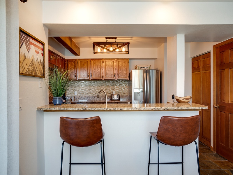 Gather at the breakfast bar and savor your morning coffee in this fully equipped kitchen with warm wood cabinetry, granite counters, and modern appliances ready for your culinary adventures.