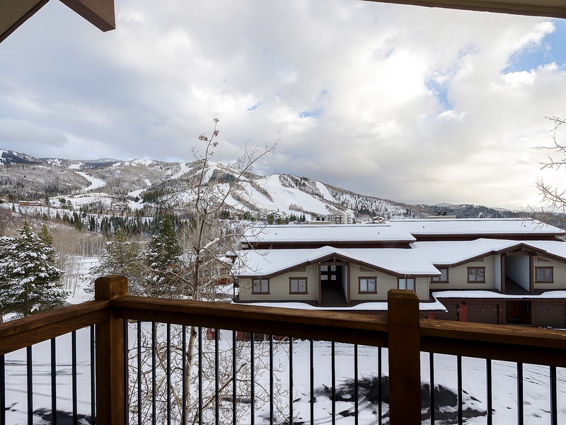 Snow-covered mountains and serene winter landscape visible from the property's balcony, framed by nearby resort buildings and evergreen trees.