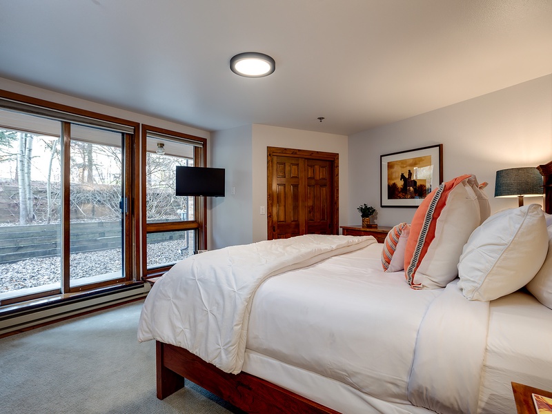 Sink into plush bedding in this serene bedroom where natural light streams through large windows, revealing tranquil outdoor views. Your peaceful mountain escape awaits.