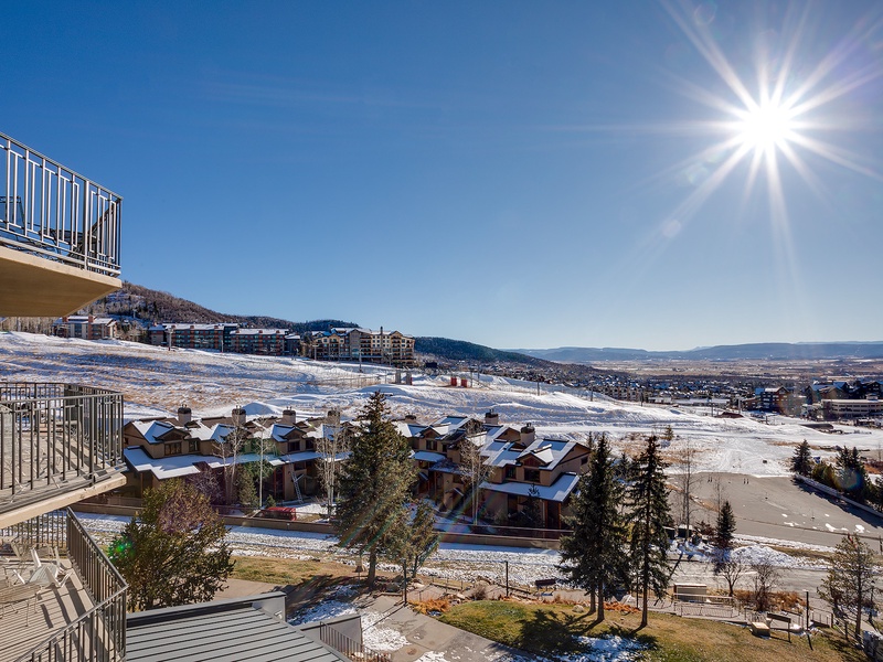 Sweeping winter panorama showcasing snow-covered slopes, neighboring residences, and distant mountain ranges under a brilliant sun. The property is located in a scenic mountain community.