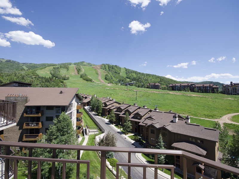 A scenic view from the property showcasing the ski slopes, surrounding mountains, and neighboring vacation homes set against a bright blue summer sky.