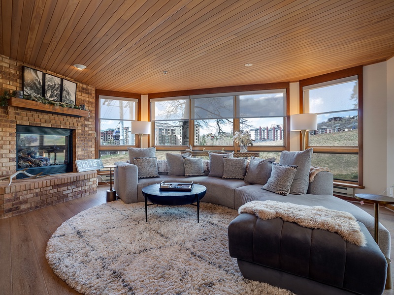 Curl up by the warmth of your fireplace in this inviting living room, where panoramic windows frame stunning views and plush seating invites you to unwind in style.