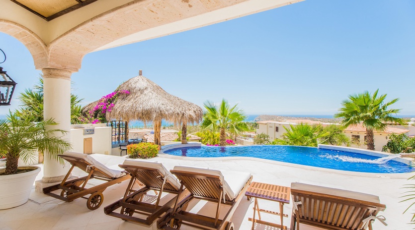 Covered patio lounge chairs and pool with ocean view