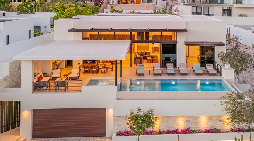 Stunning modern villa showcases contemporary design with terraced levels, infinity pool, and warm evening lighting in an upscale hillside neighborhood.