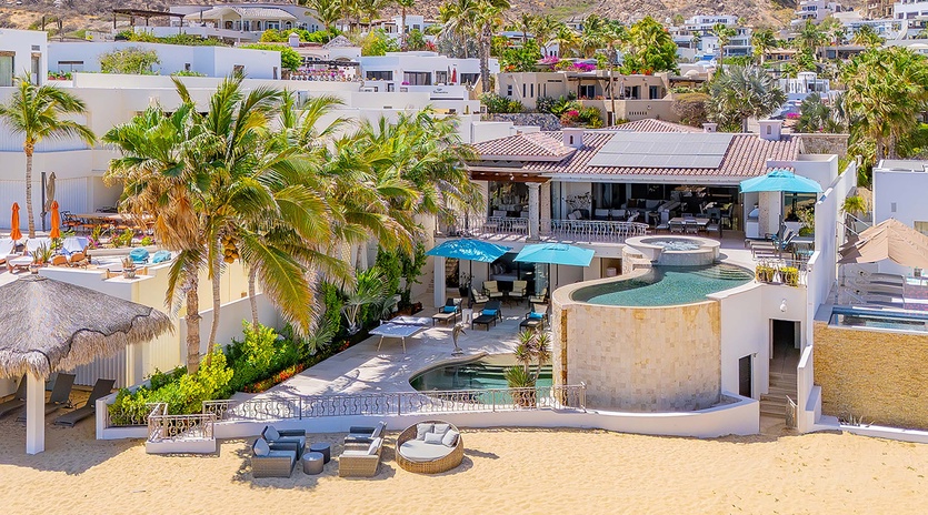 Hillside beachfront villa showcasing multi-level pools, private sandy beach access, tropical palms, and sunny outdoor lounging areas in an exclusive coastal neighborhood.