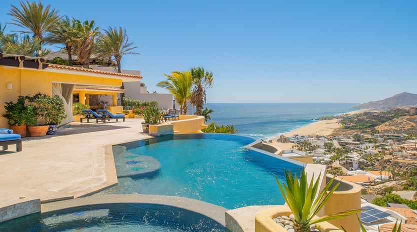Stunning infinity pool overlooking azure waters and golden coastline, surrounded by tropical palms and luxurious outdoor lounging spaces.