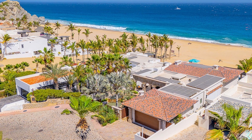 Aerial view of beachfront property nestled among swaying palms, overlooking golden sand and turquoise waters. A stunning coastal setting with dramatic rocky cliffs and endless ocean horizons.